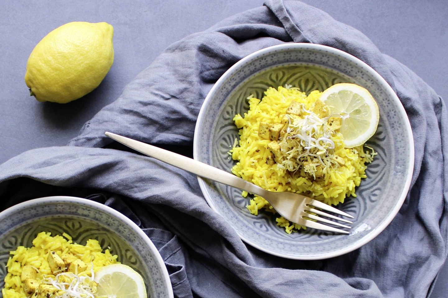 Lemon rice with tofu in patterned bowls with a fork and garnished with lemon wedges
