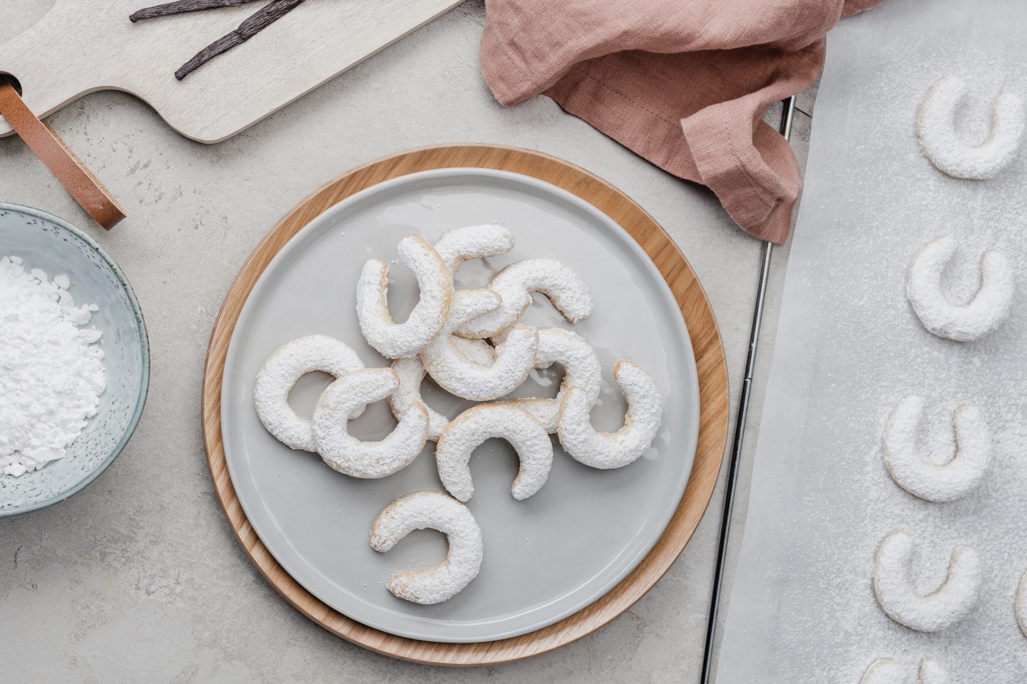 Vanilla kipferl on a light gray plate, next to it a tray with more vanilla kipferl