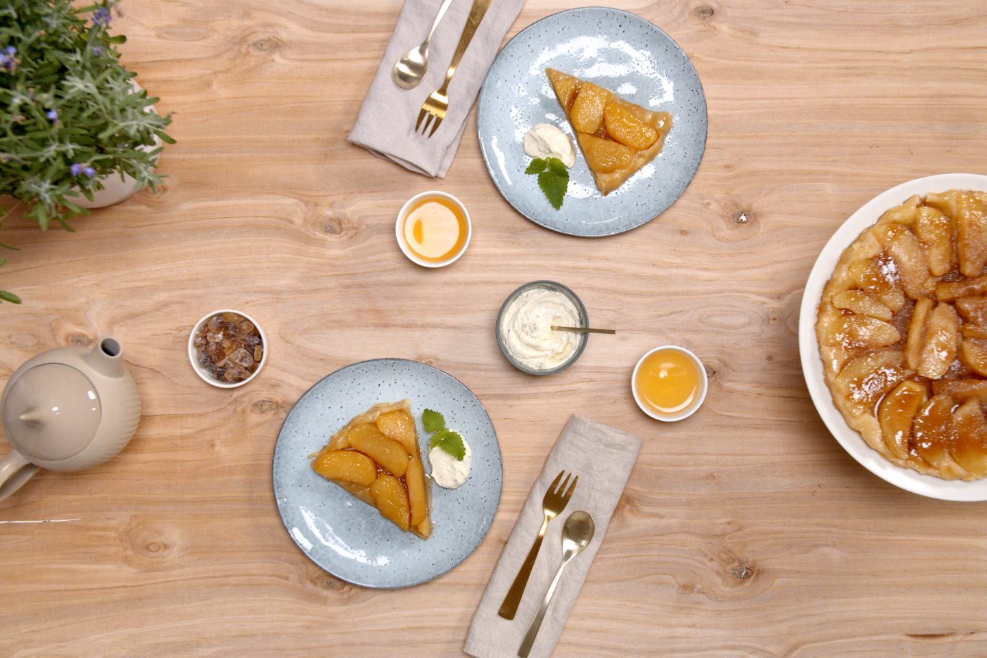 2 pieces of tarte tatin on light blue plates, next to the whole cake on a white cake stand