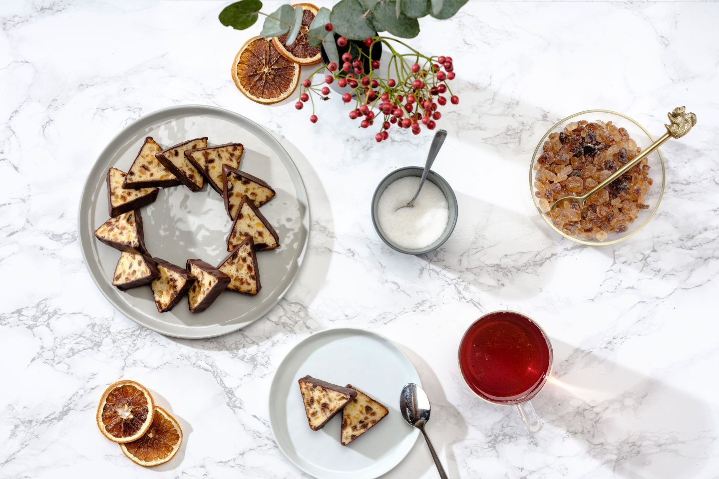 Tea cake in the shape of a wreath on a gray plate arranged with a cup of tea, rock sugar and rowan berries on a marble background